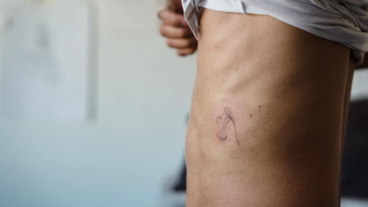 Close-up view of a minimalist tattoo on a person's side torso in an indoor setting.