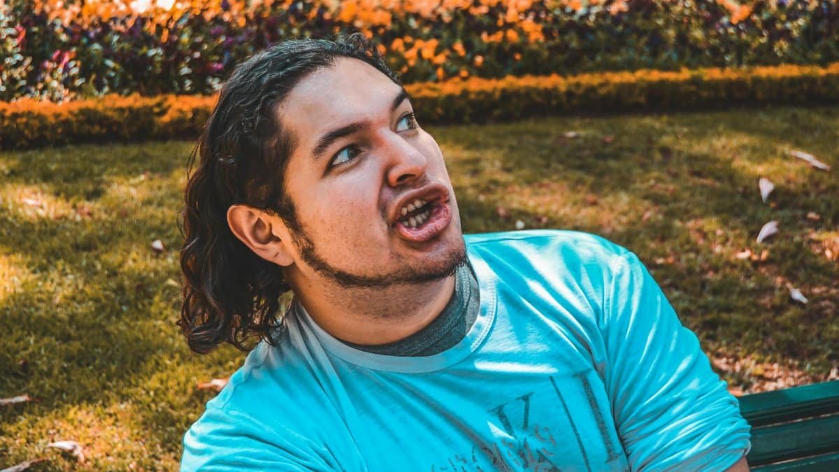 A man with a playful expression posing in a sunlit park, showcasing an amusing moment outdoors.