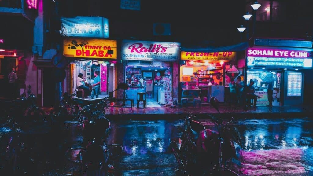 Colorful street scene in Kolkata with glowing shop signs and wet pavement at night.