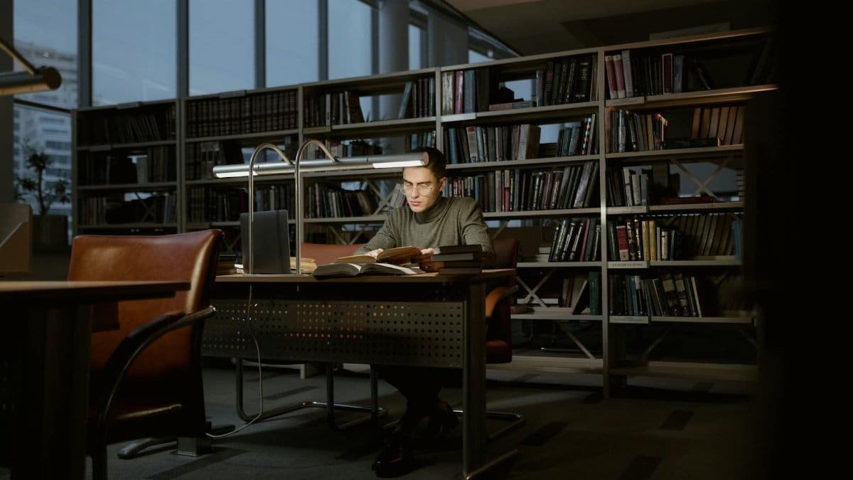 A man intensely studies in a quiet library, surrounded by books and soft lighting.