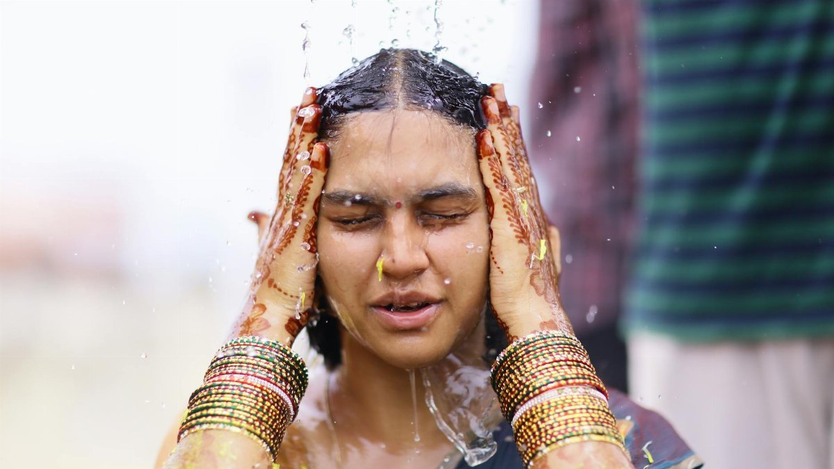 A woman participates in a traditional Indian water ritual, adorned with henna and vibrant jewelry.