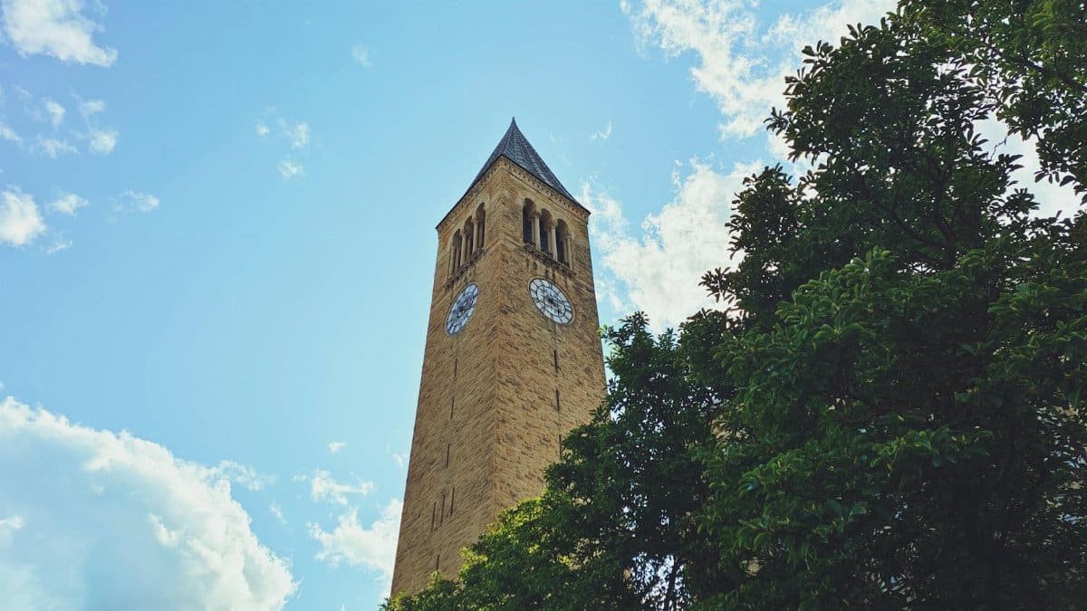 Low angle view of McGraw Tower at Cornell University in Ithaca, with clear blue skies and trees.