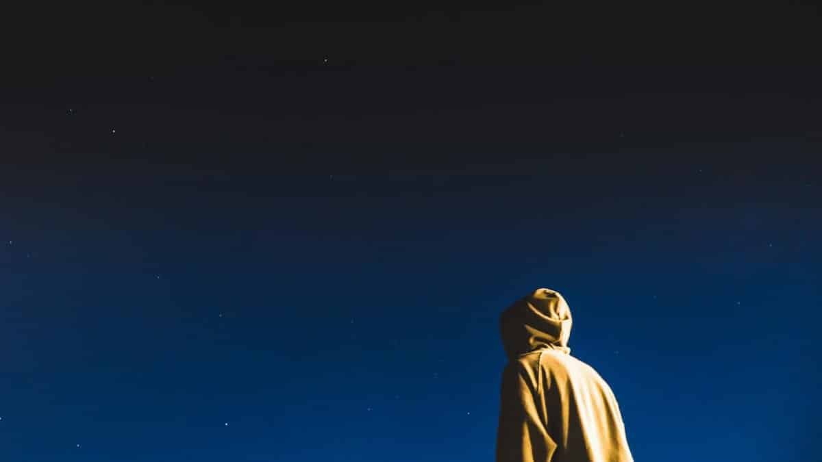 A person in a hoodie looks up at the starry night sky, capturing a moment of solitude and wonder.