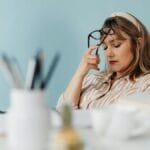 Caucasian woman looks exhausted while taking a break with eyes closed at her desk.