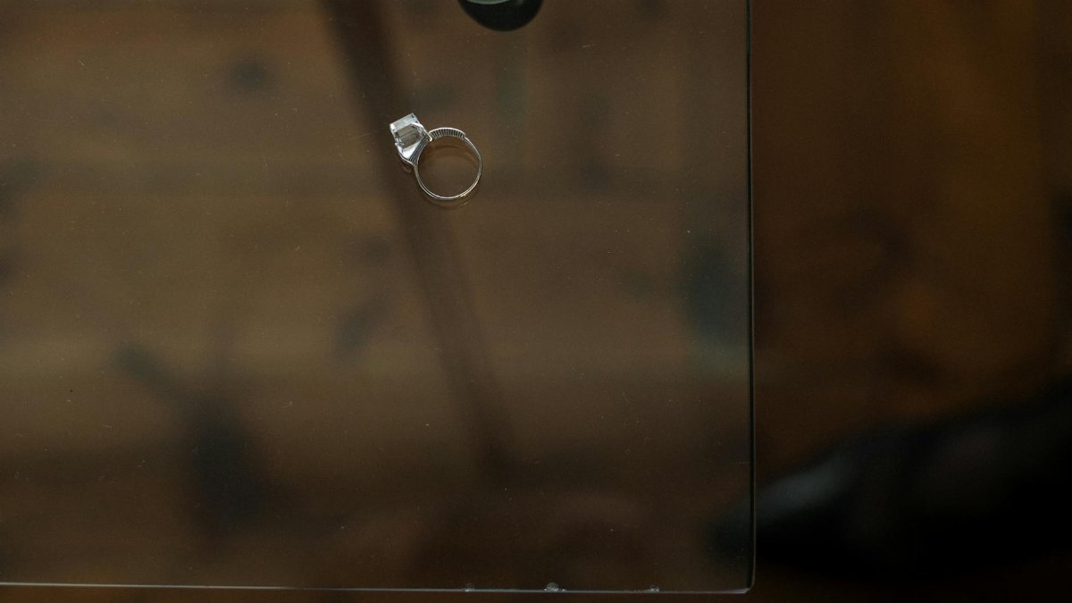 A single engagement ring rests on a glass table, symbolizing relationship reflection.