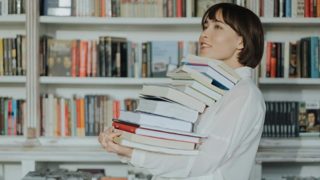 A woman joyfully holds a pile of books in a library, embodying the love of reading and learning.