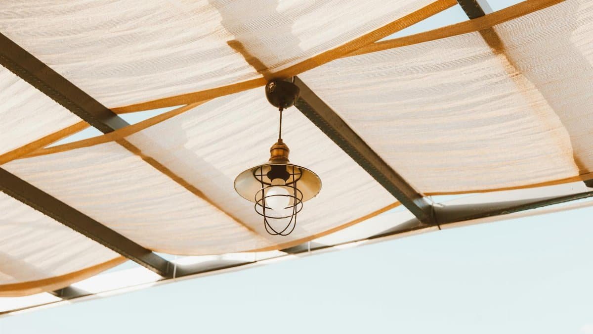 Minimalist industrial lamp hanging under a fabric ceiling against a clear blue sky.