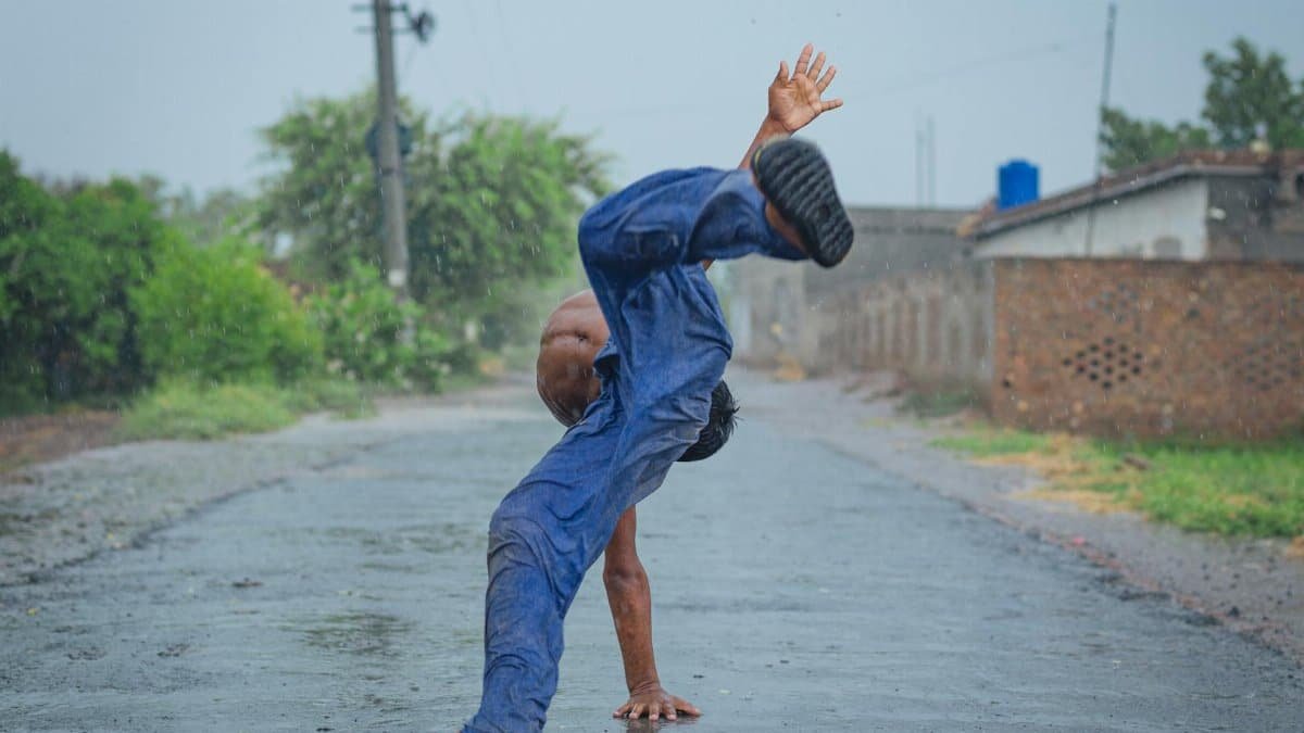 A man performing an energetic dance move on a wet street during rain.