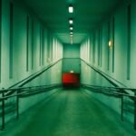 A long, empty corridor with dim lighting and an accessibility ramp leading to a red door.