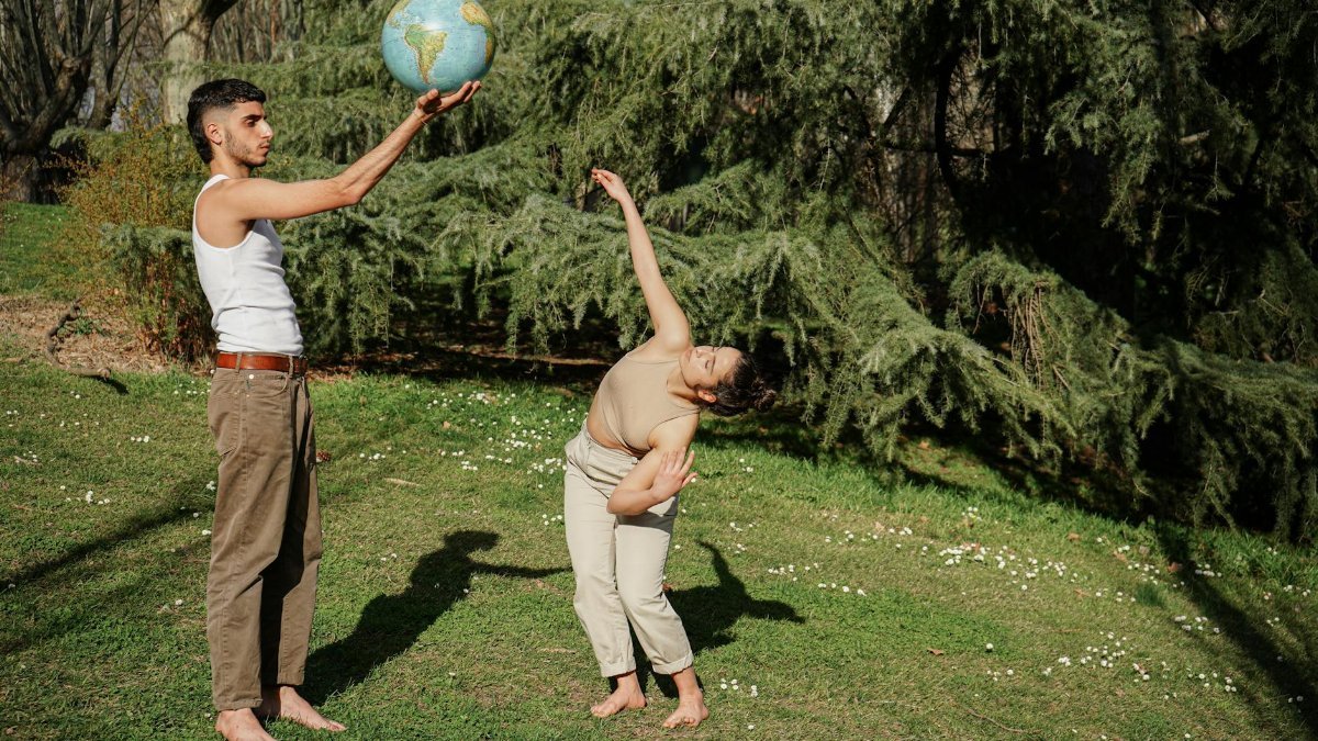 Two people in a park embody an Earth-friendly concept with creative poses and a globe.