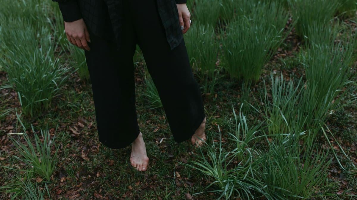 A person standing barefoot in grass, embracing nature with tranquility.