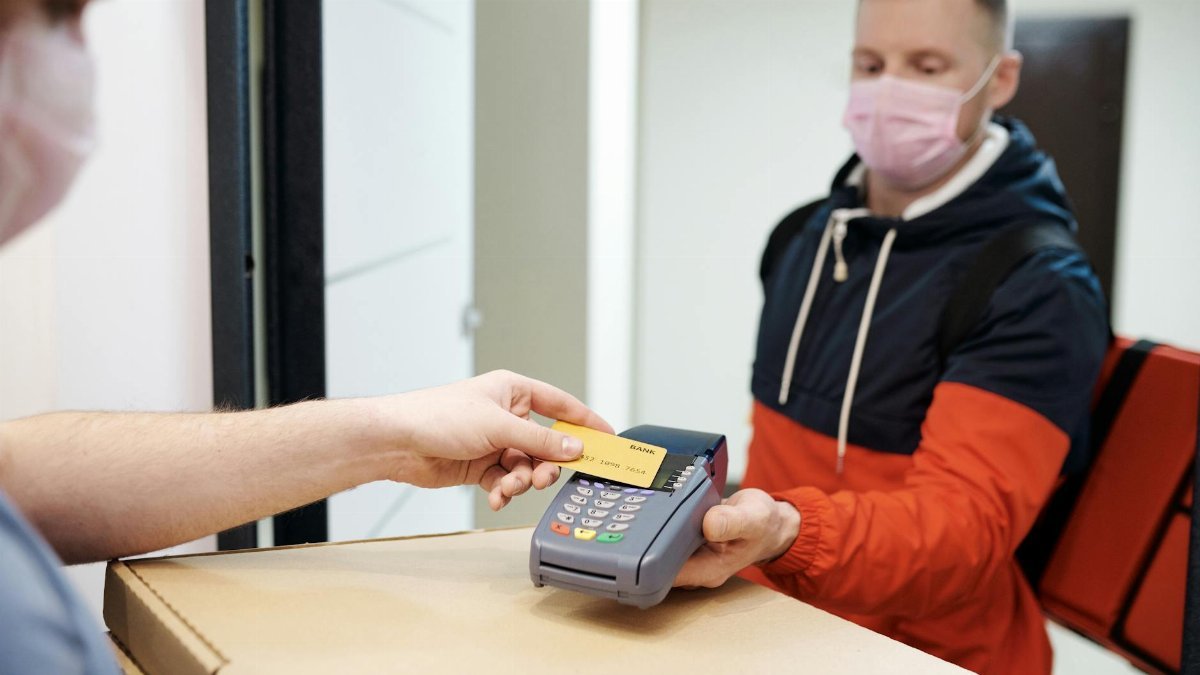 A man making a contactless payment for food delivery, both wearing face masks for safety.