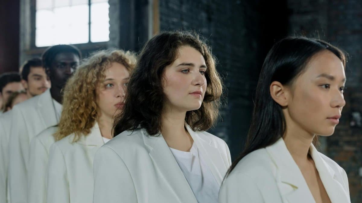 A diverse group of people standing in line indoors, wearing white outfits, with a focus on unity and harmony.