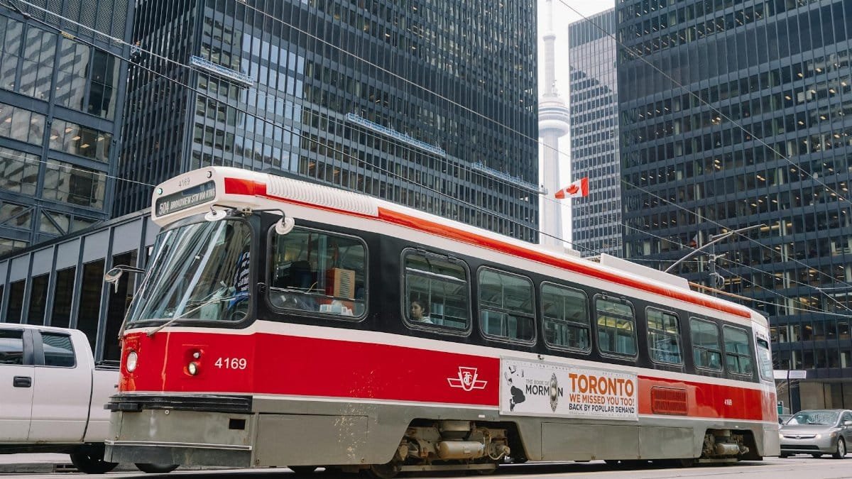 Red public tram on railroad in middle of megapolis roadway surrounded with high rise buildings