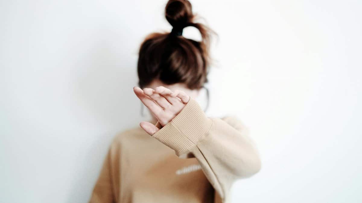 A woman in a sweatshirt raises her hand to cover her face, suggesting stop or privacy.