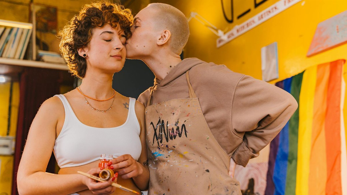 Two young women embrace creativity and love in an artistic studio setting.