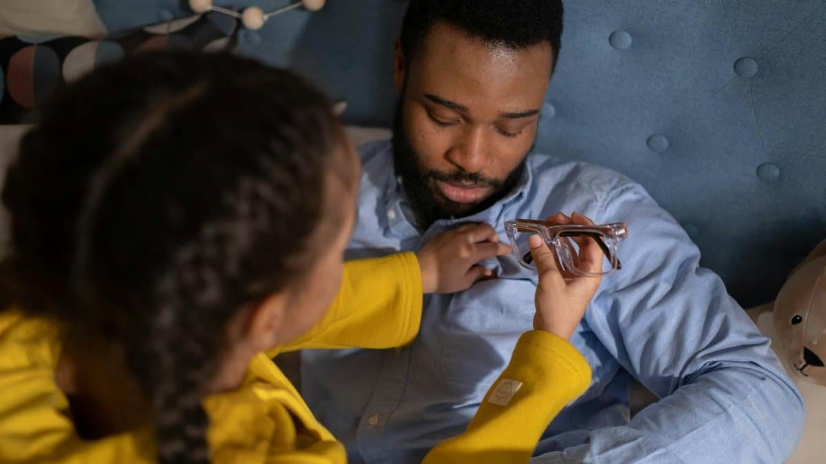 A father and daughter enjoying quality bonding time indoors on a bed with eyeglasses.