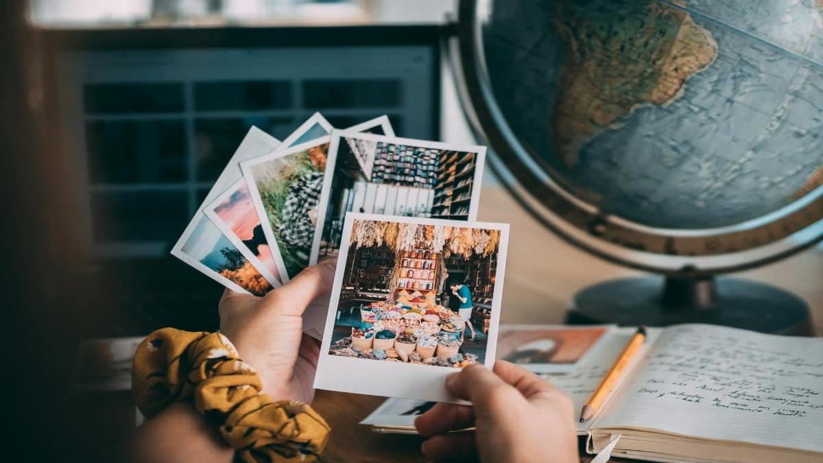 Hands holding Polaroid photos with a globe and journal, evoking travel memories.