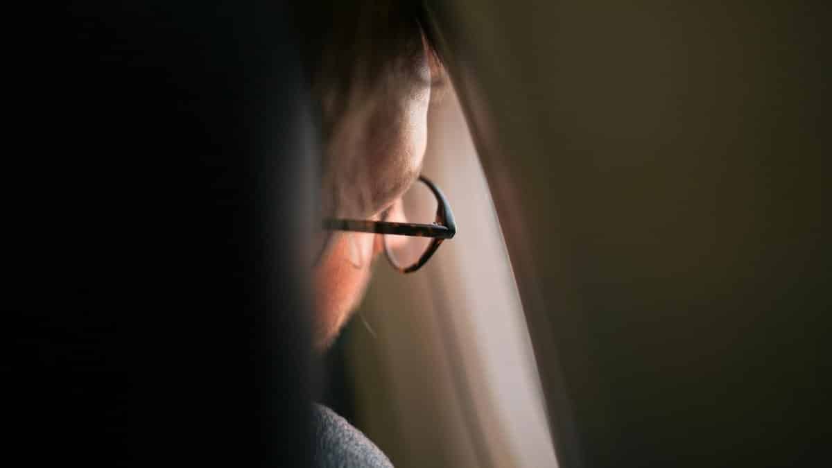 A thoughtful man gazing out an airplane window, wearing eyeglasses, in soft ambient lighting.