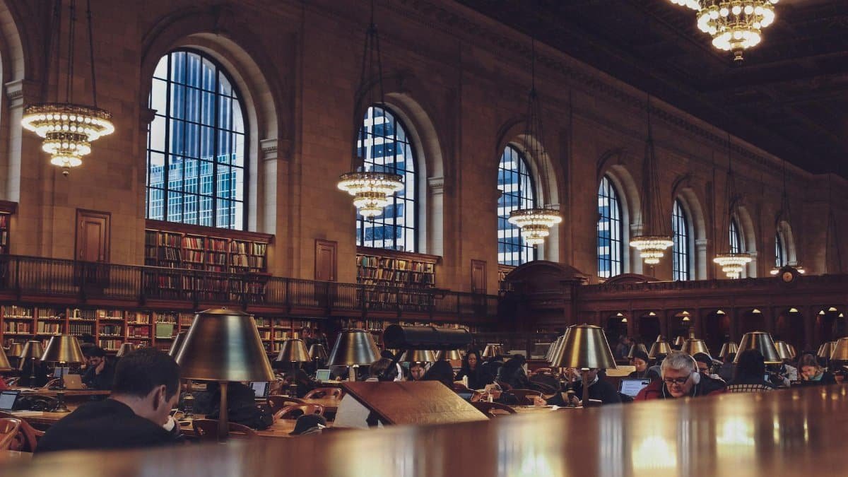 Interior view of a bustling reading room with chandeliers at the New York Public Library.