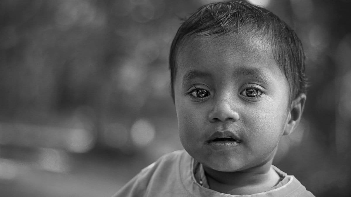 Close-up black and white portrait of a young boy with expressive eyes in soft focus.
