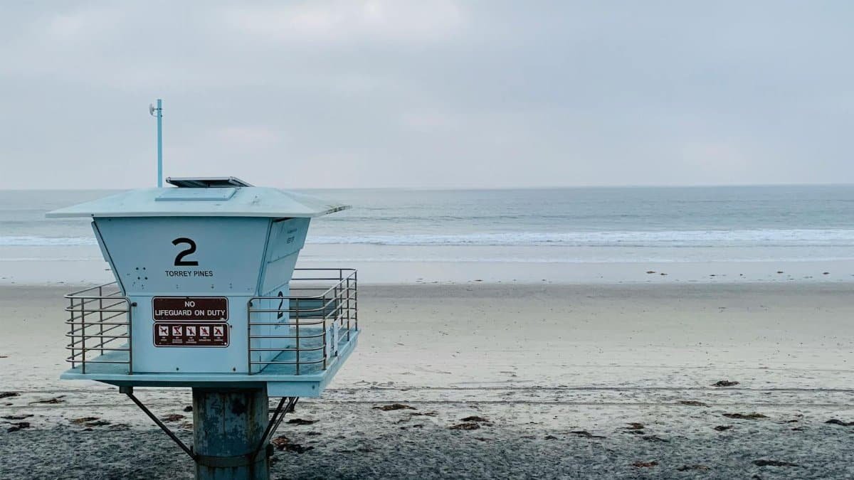 Small modern lifesaver house on sandy beach near calm rippling sea beneath cloudy overcast sky in twilight