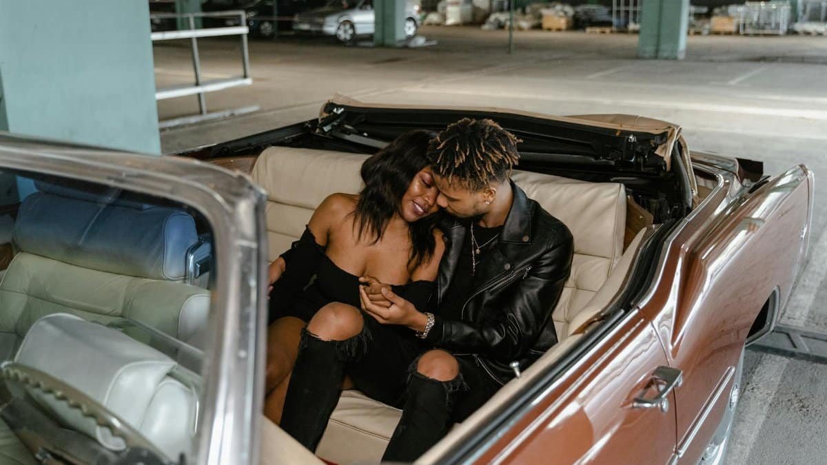 A loving couple sharing a tender moment seated in a vintage convertible car.