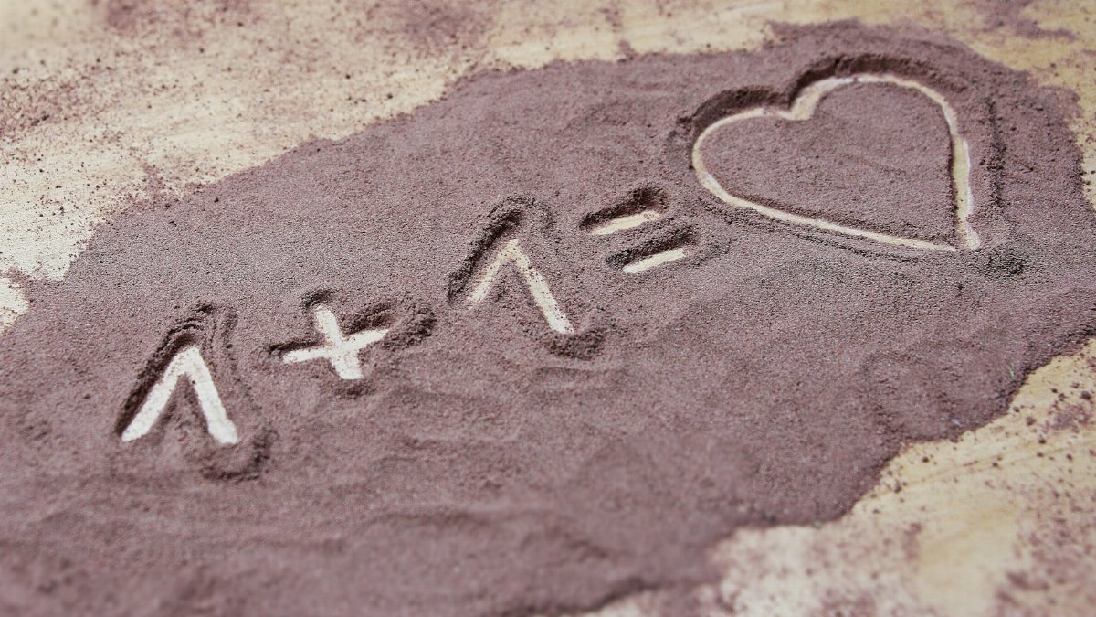 Equation written in sand with 1+1 equals heart. Expresses love and creativity.
