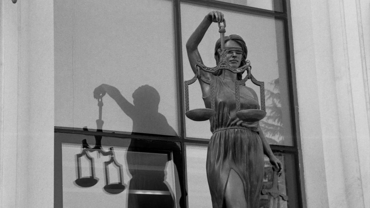 Black and white image of Lady Justice statue reflecting in a window, symbolizing fairness.