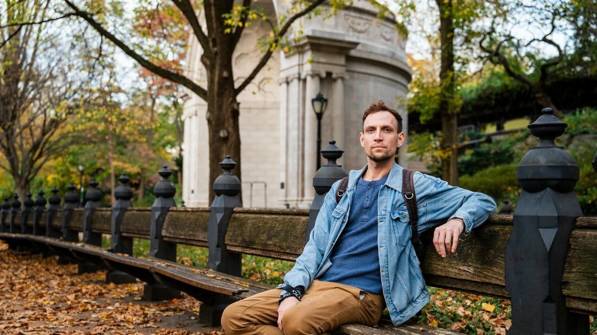 A man sits on a wooden bench in Central Park, New York, during autumn.