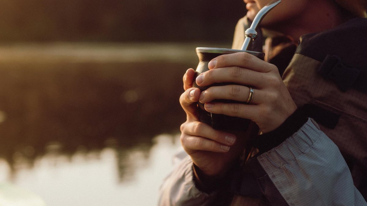 A serene scene of a person enjoying yerba mate by a lake during sunrise, savoring the tranquil morning.