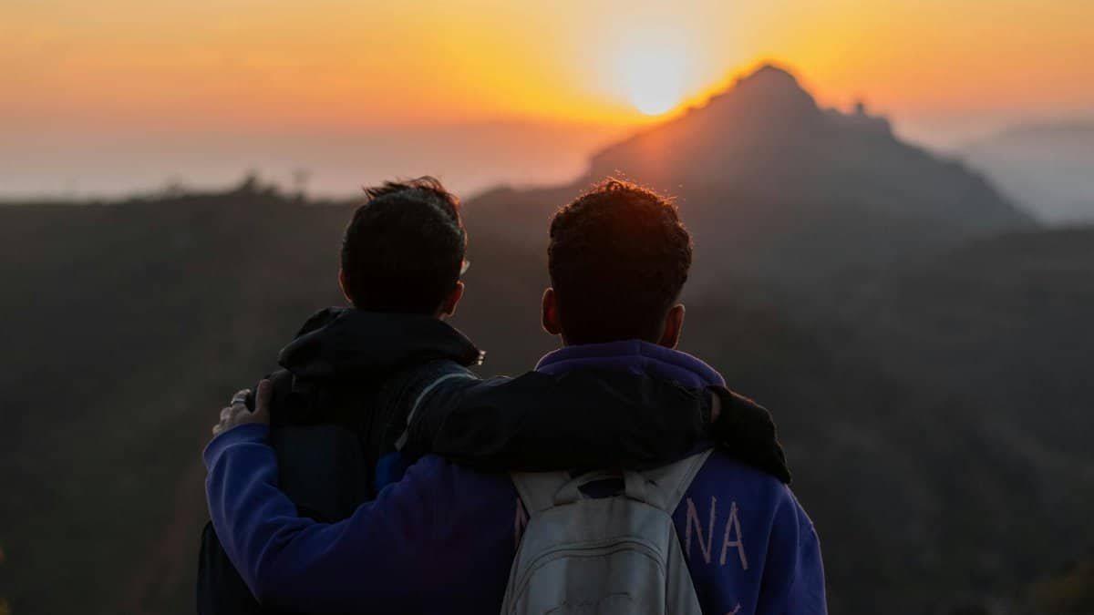 Two friends embrace at sunrise, overlooking a misty mountain landscape, symbolizing friendship and adventure.