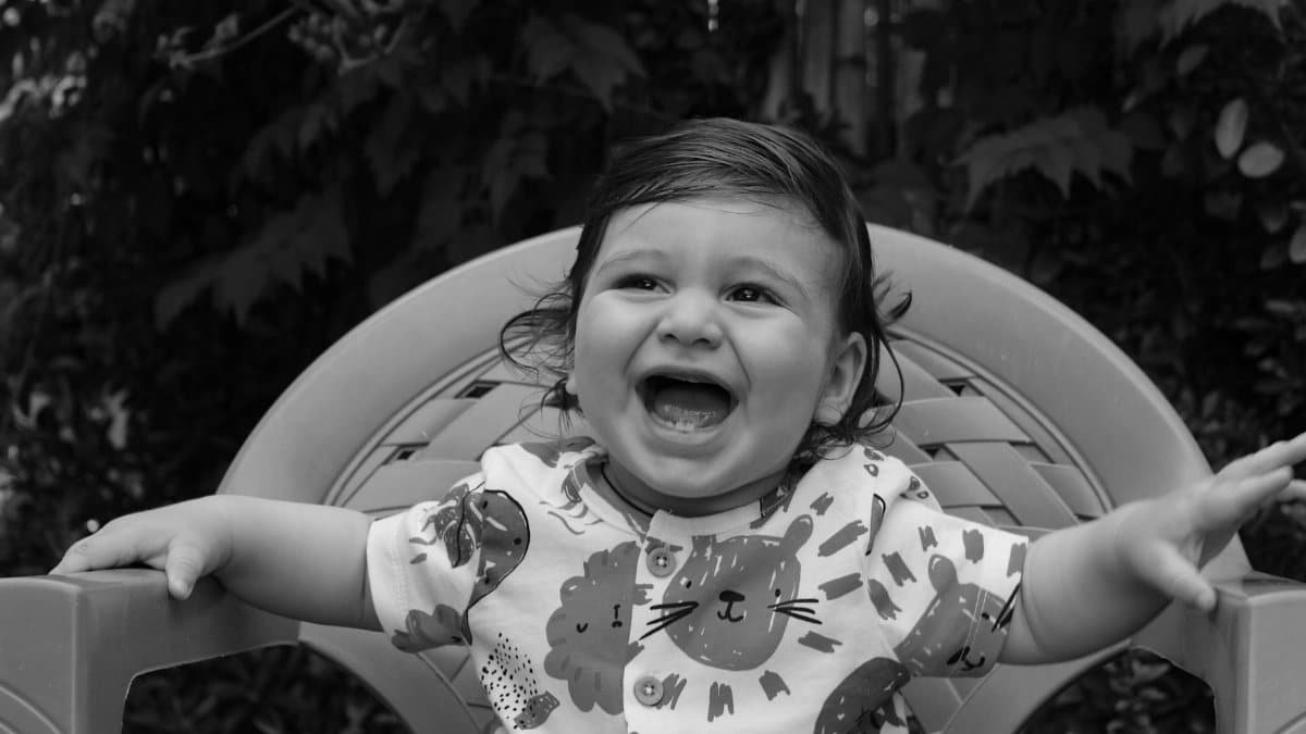A grayscale portrait of a happy baby smiling and sitting in a chair outdoors.