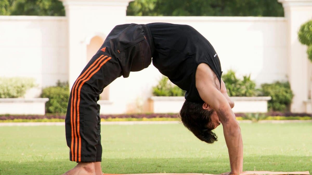 A man practicing a backbend yoga pose on grass in a serene outdoor setting.