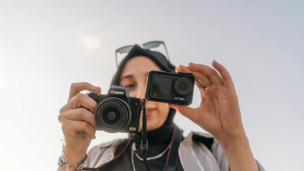 A female photographer showcases two different cameras under a clear sky, depicting modern photography technology.