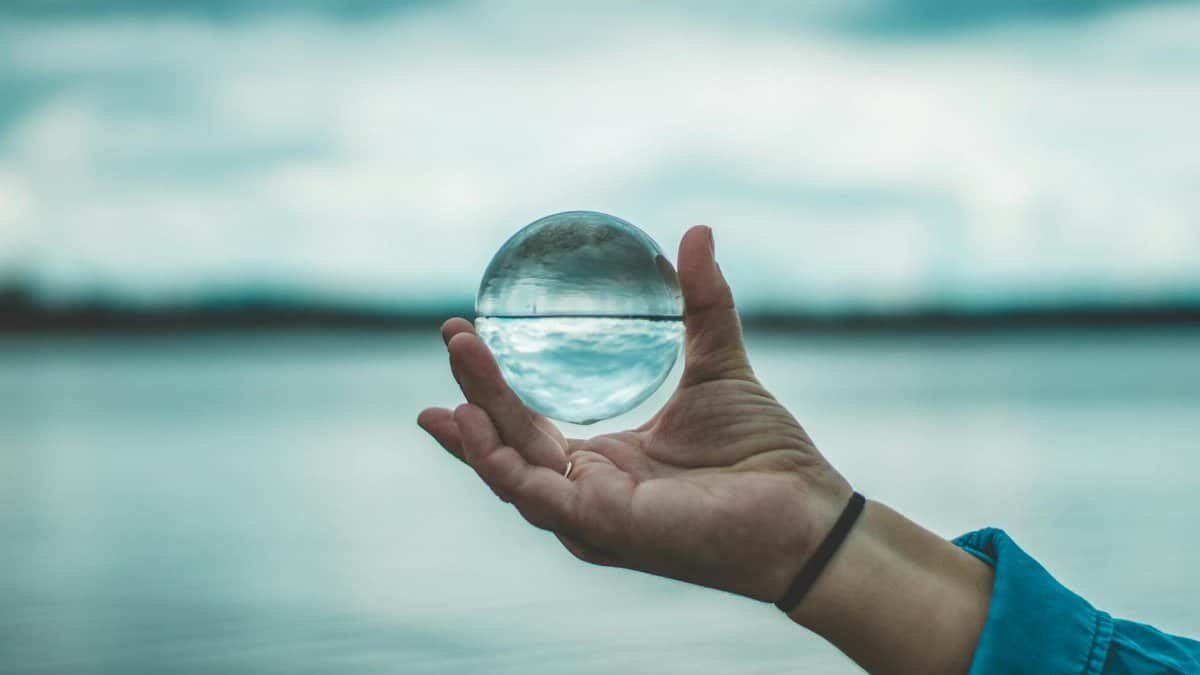 A hand holding a glass sphere reflecting a serene lake and sky, creating a dreamy visual effect.