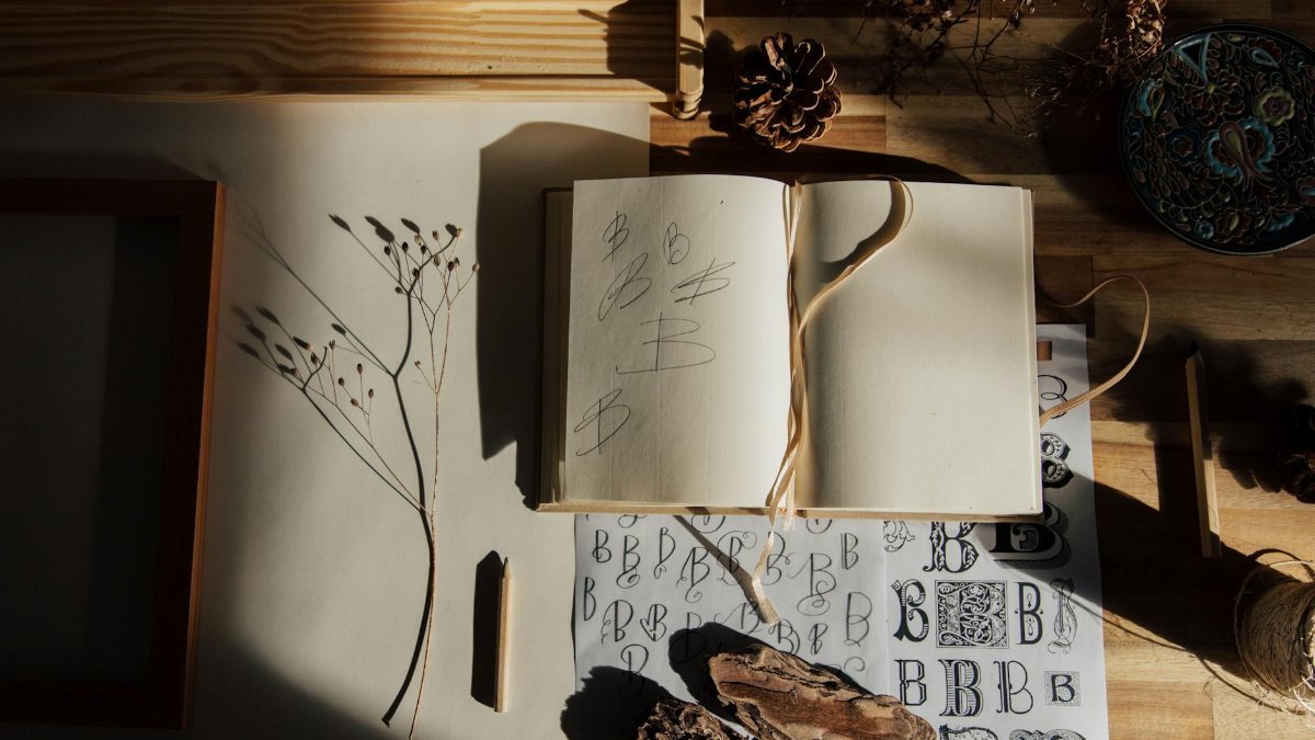 Top view of opened notebook with pencil and dried flower placed on wooden table near other decorative elements illustrating handwriting practice as hobby
