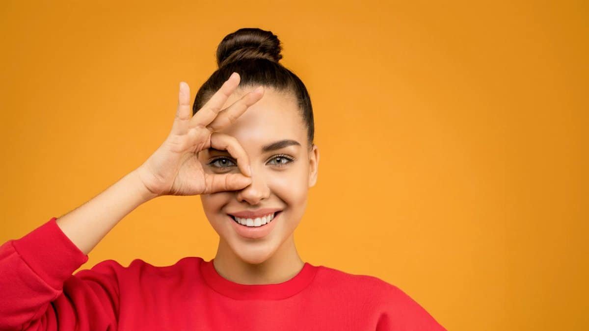 Smiling woman making a playful hand gesture against a vibrant orange background.