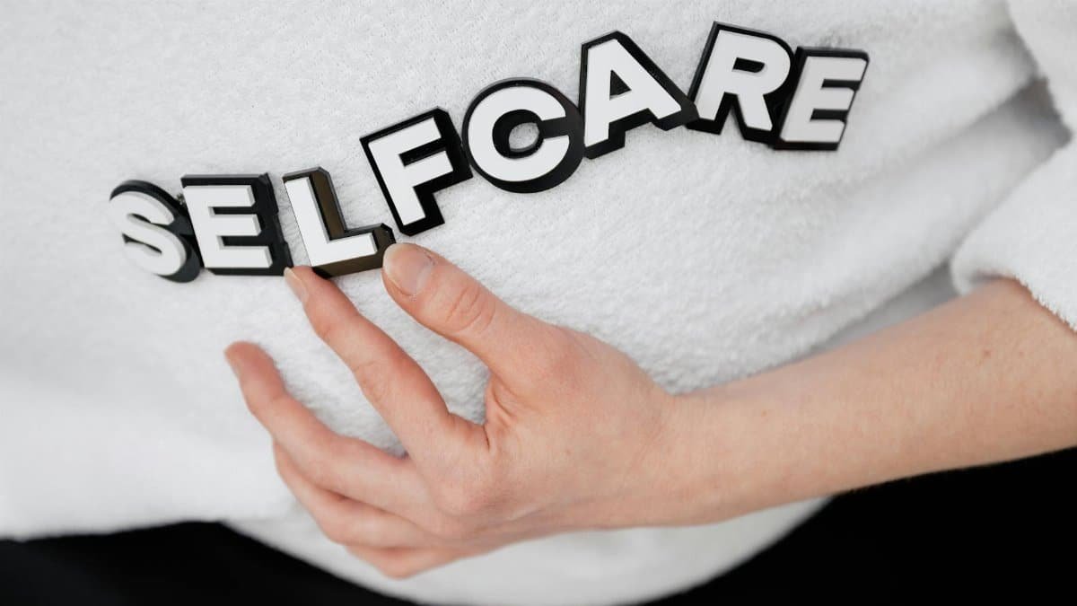 Close-up of a hand holding the word 'self-care' made with 3D letters on a white background.