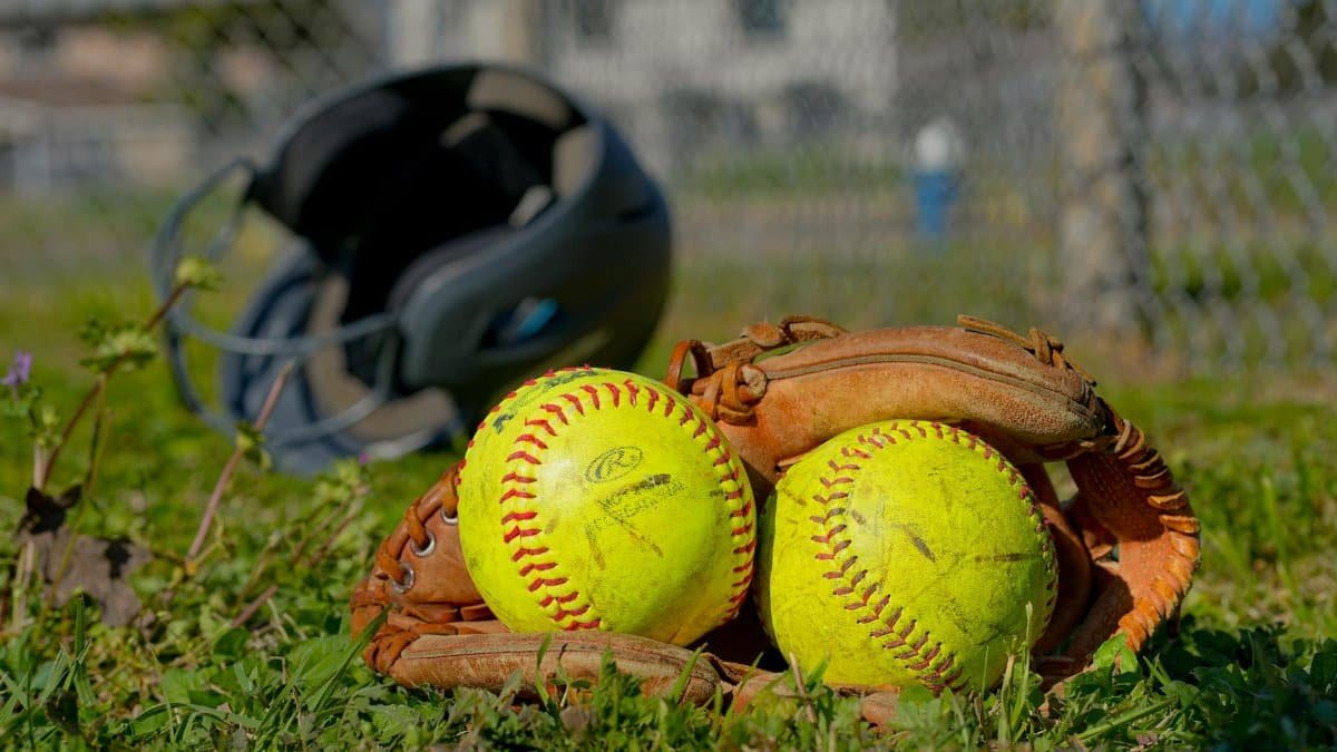 Close-up of baseball gear including balls, glove, and helmet on a field in Houston, TX.