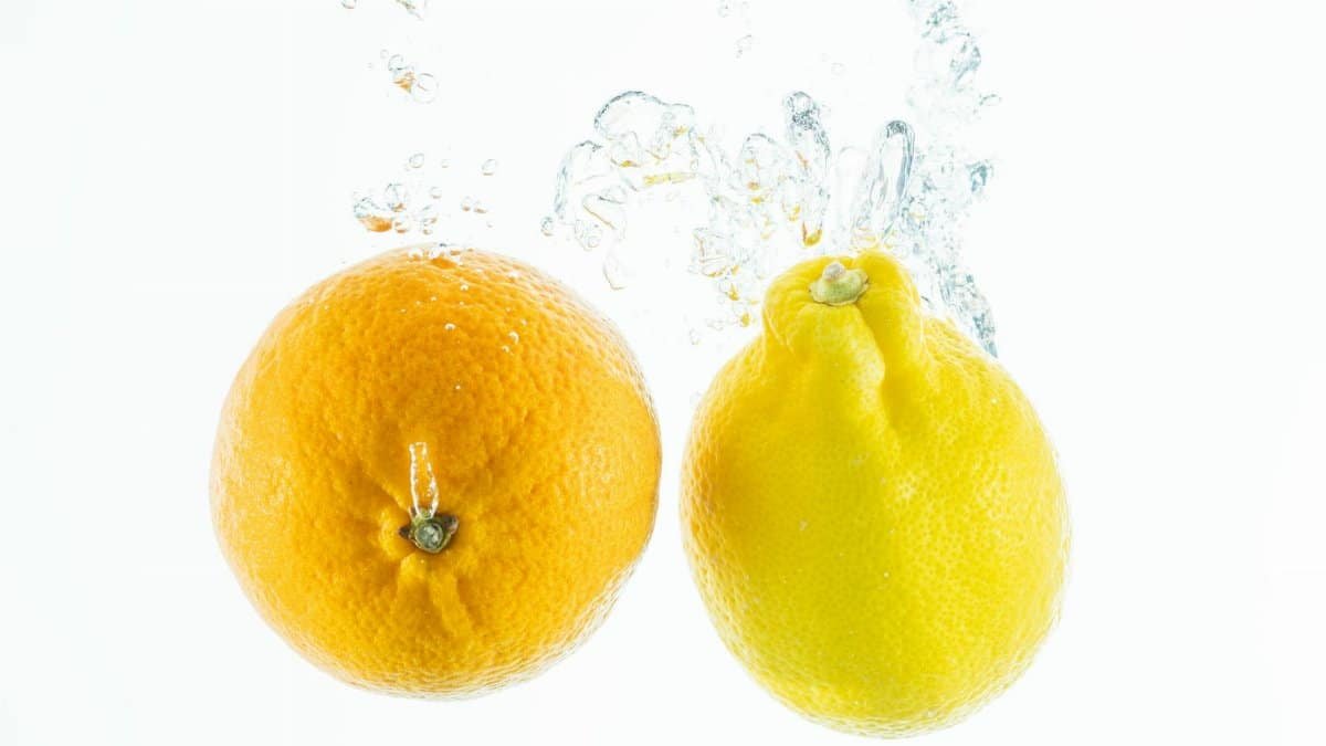 Orange and lemon splash into water, showcasing freshness and vitality on a white backdrop.