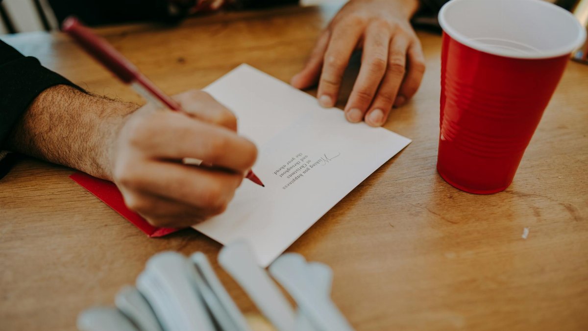 Close-up of hands writing a letter at a cozy home setting with a red solo cup and utensils.