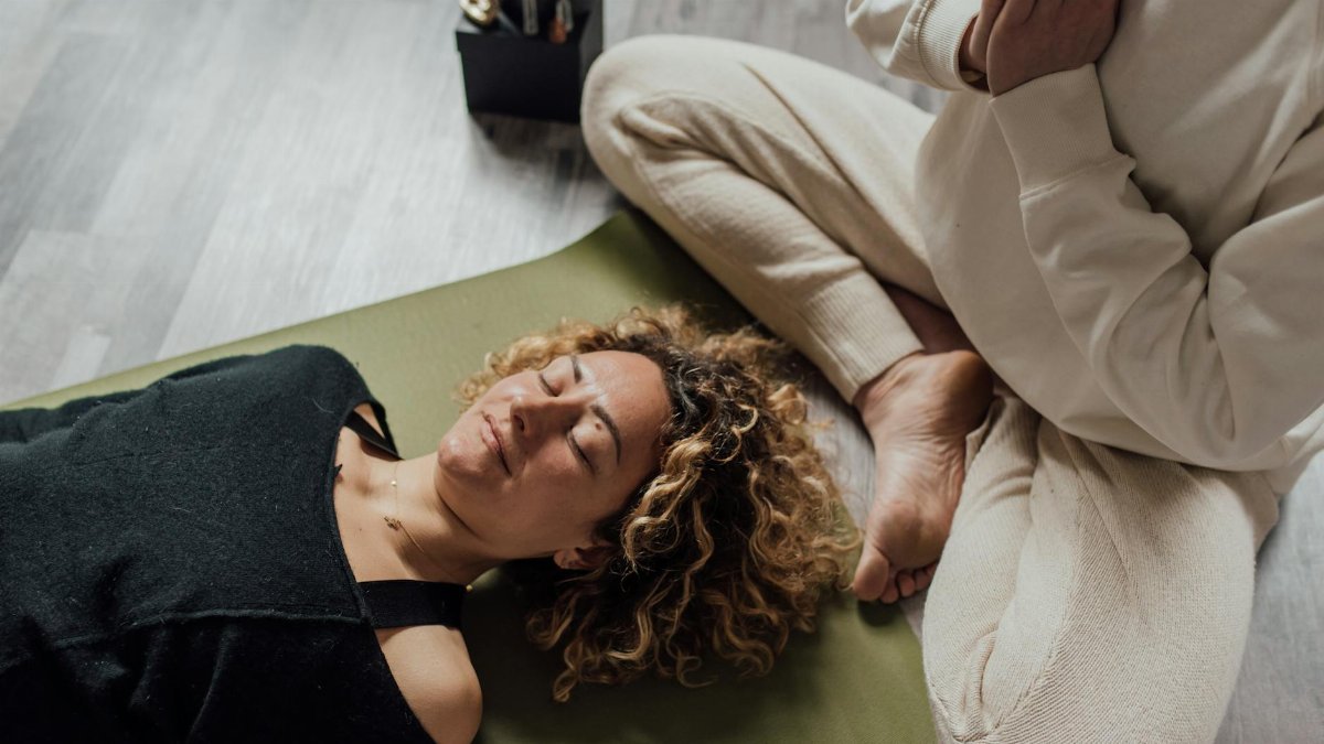 Relaxed woman meditating on yoga mat with another person praying beside her indoors.