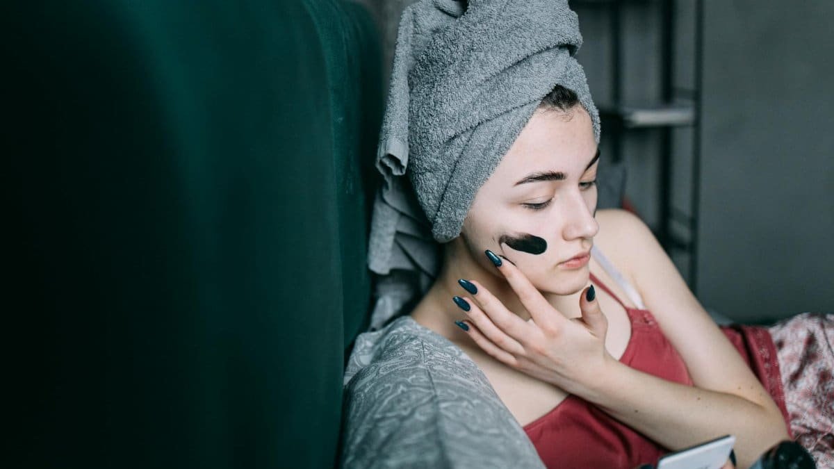 Woman at home applying a facial mask for relaxation and skincare. Self-care routine with a towel on head.