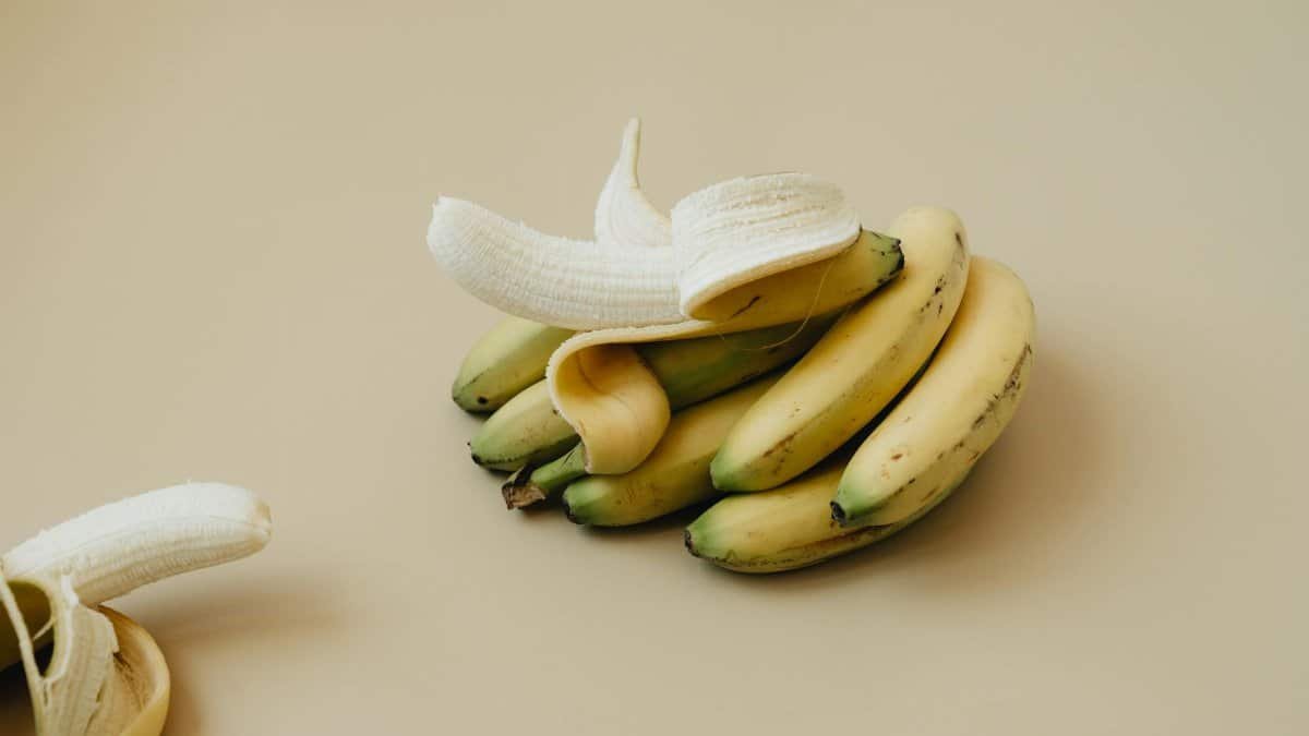 A bunch of ripe bananas with one peeled, displayed on a neutral backdrop. Ideal for food visuals.