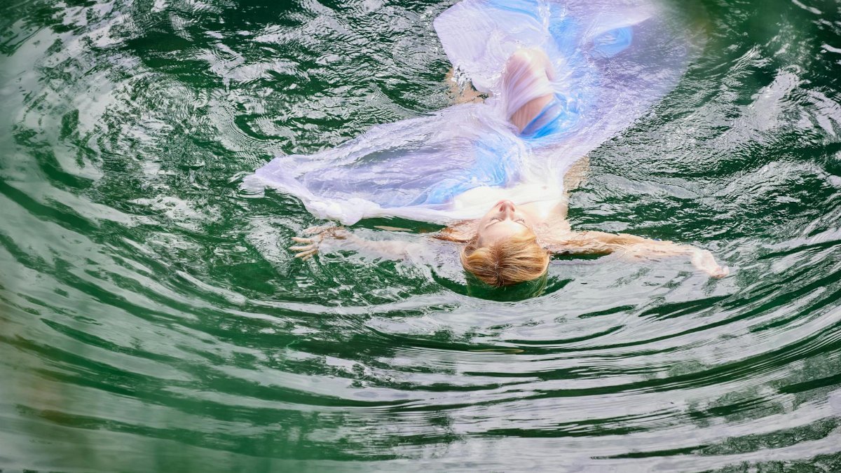 A woman in a flowing dress floats gracefully in tranquil water, capturing a moment of relaxation.