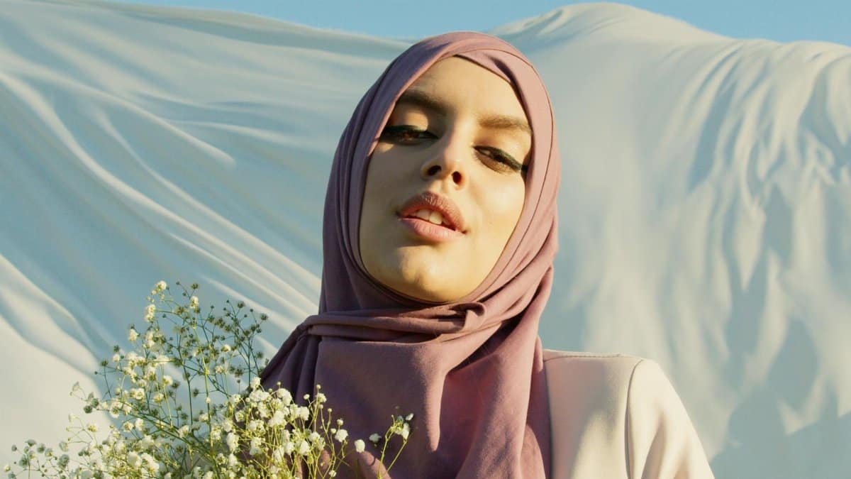 A beautiful woman in a hijab, smiling gently with baby's breath flowers against a flowing white background.
