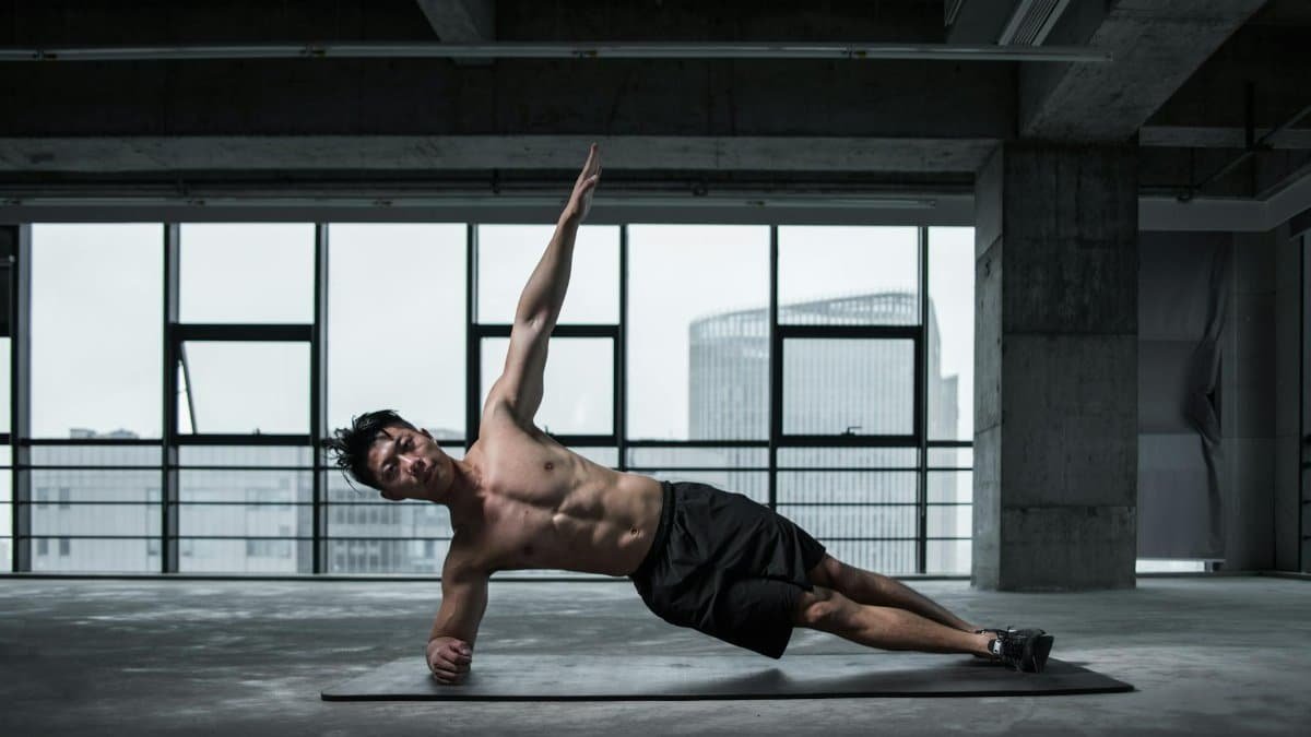 Fit man doing a side plank in an urban indoor gym, showcasing core strength and balance.