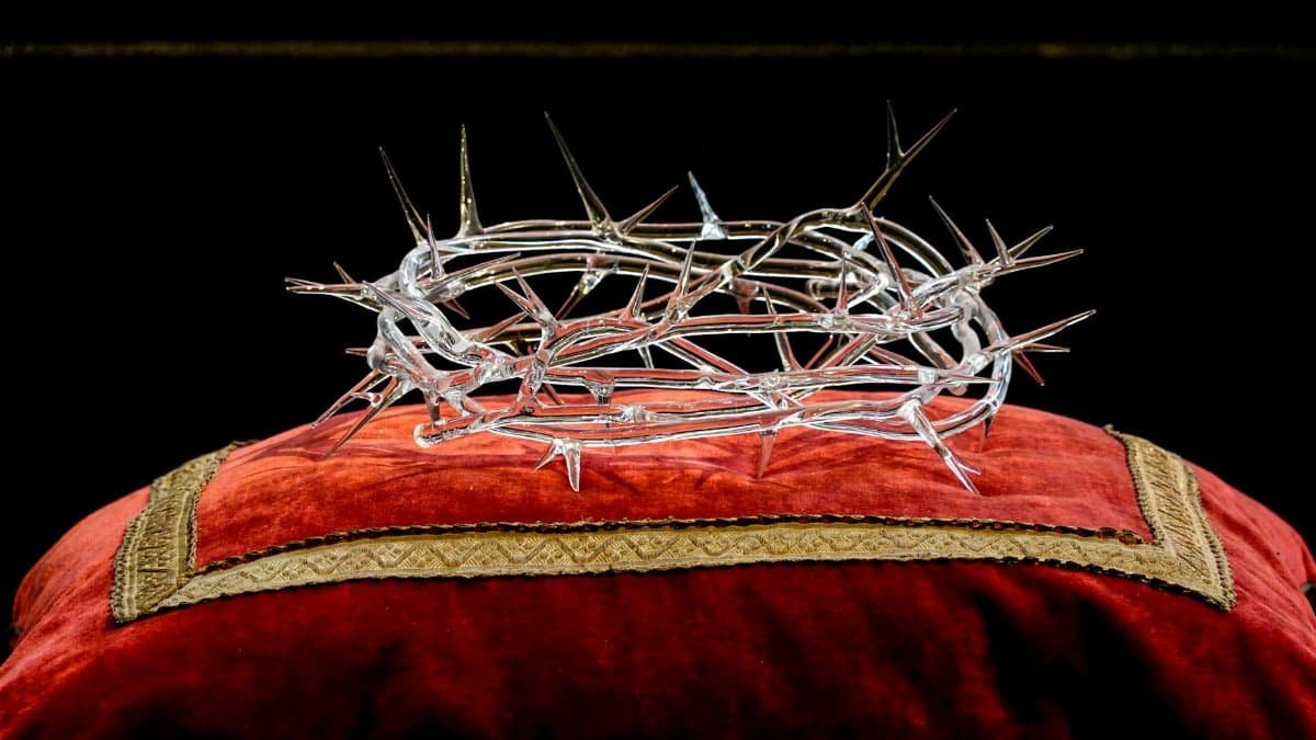 Intricate glass crown of thorns resting on a luxurious red velvet cushion.
