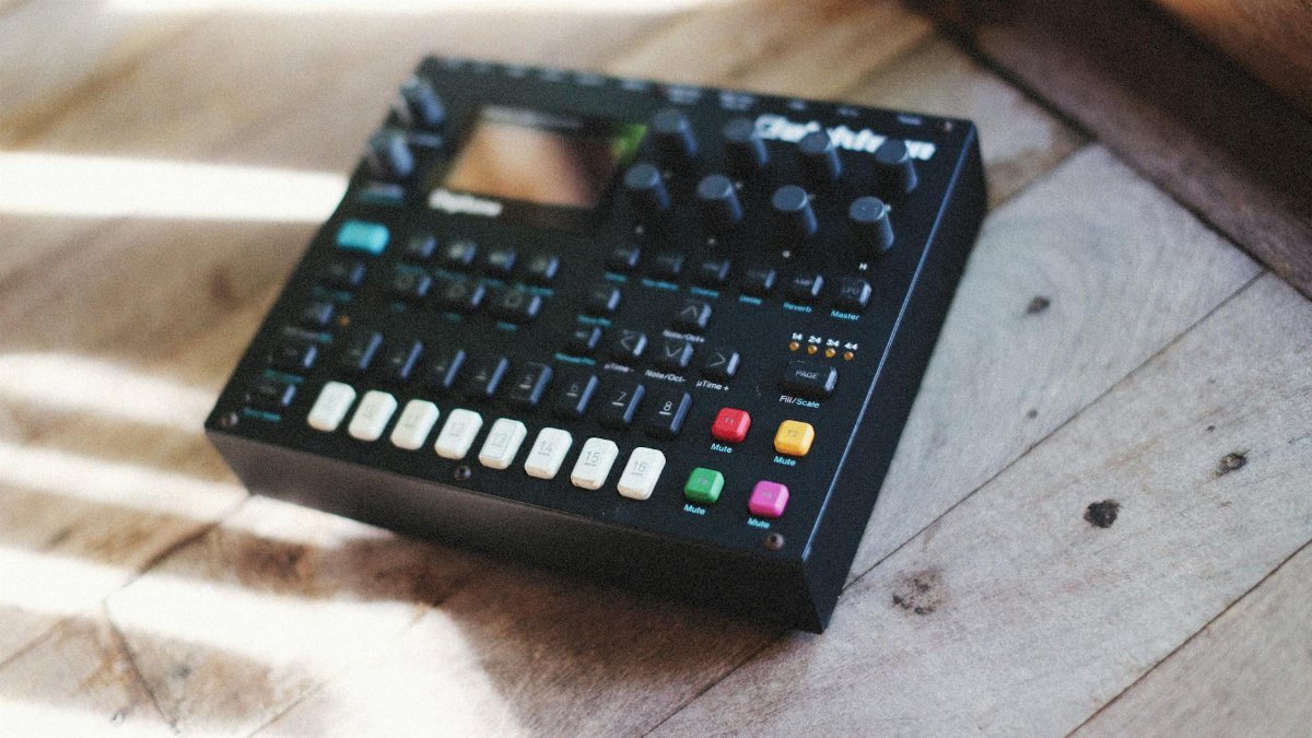 Close-up of a digital synthesizer with colorful knobs on a wooden floor, lit by sunlight.